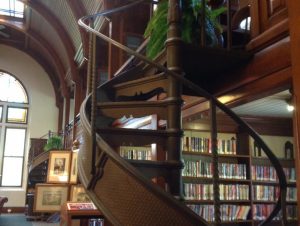 Spiral staircase with plant at top in foreground and shelves of books in background