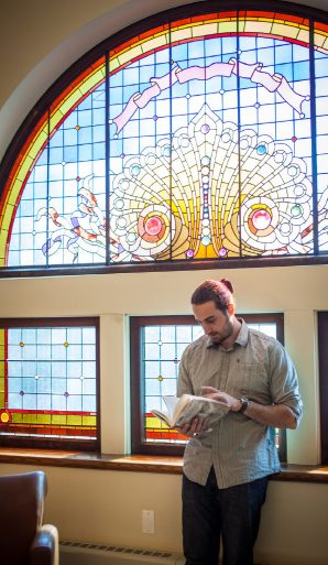 A picture of a man reading in front of dyed glass.