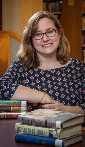 A woman smiling next to a pile of books