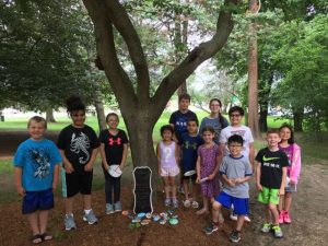 Group of children standing next to a tree, and under the tree are a bunch of kindness rocks