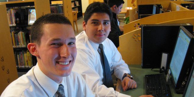 Two young men smiling in front of computers
