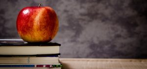 Apple on a pile of books with a chalkboard behind it