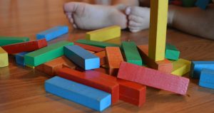 Multi colored blocks in a pile in the foreground with two baby feet in the background