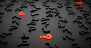 Black question marks with three orange question marks scattered on a black table