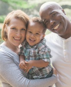 A dark skinned man, a light skinned woman, who is holding a tanned skinned young boy