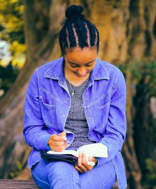 A young dark skinned woman reading a book with a pen in her hand