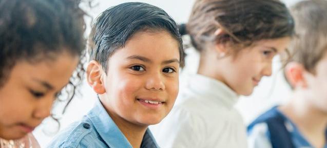 Child smiling at the camera while others look down at their work