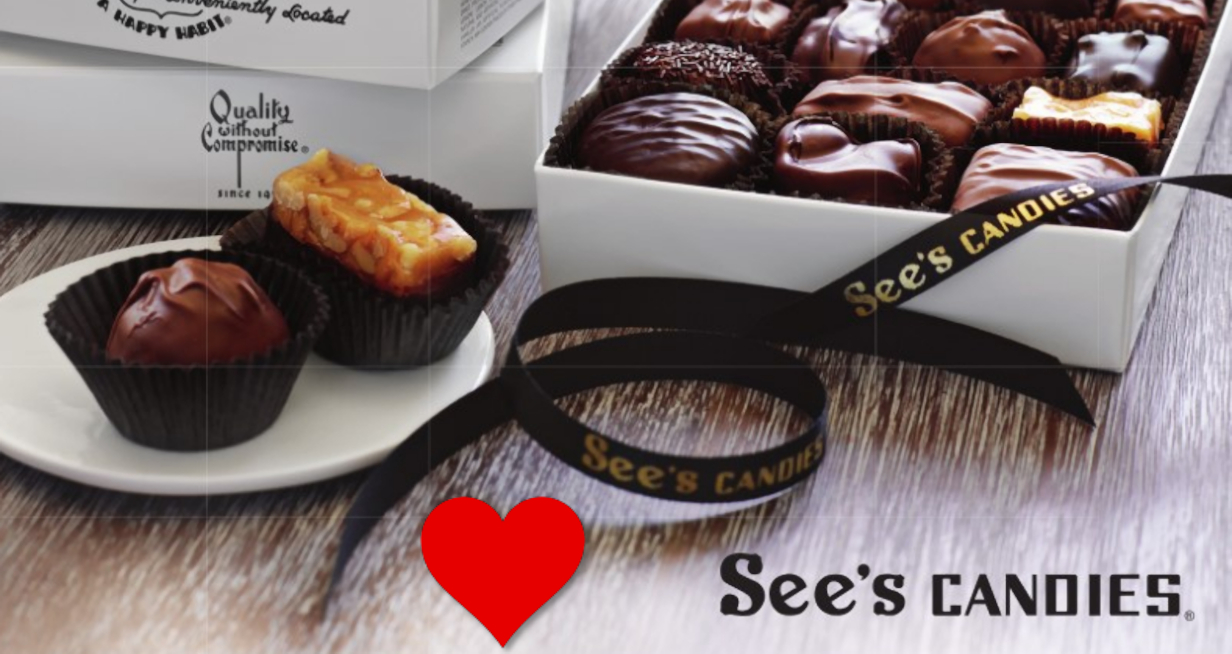A chocolate and caramel candy on a plate on the left with a box of various chocolate candies to its right and below both a red heart and the words See's Candies