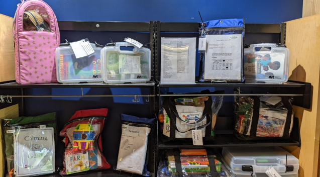 Shelving with a variety of kits in boxes and bags on it.