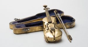 Small metal golden colored violin and bow leaning against a case with blue on the inside