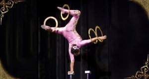 Acrobat in pink leotard balancing on one hand while spinning rings around other three extremities