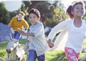 A girl and a boy with smiles on their faces being chased by their smiling babysitter