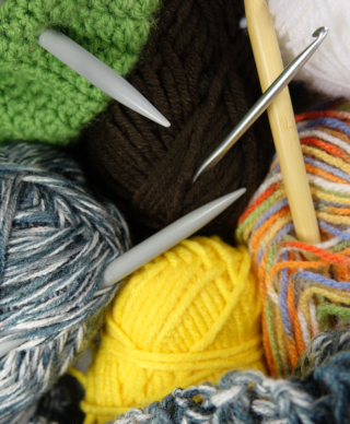 Pile of multicolored wool skeins with knitting needles and a crochet needle sticking out