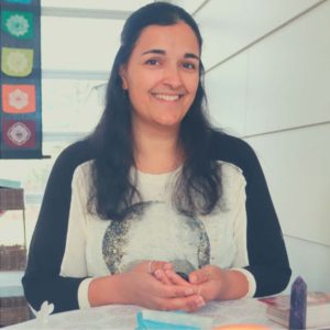 Light skinned woman with long black hair in a t-shirt and standing at a table with folded hands