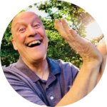 Light skinned man smiling manically and holding his hands up to the shining sun