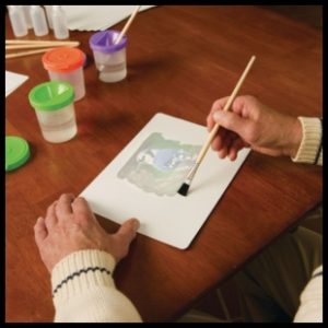 A light skinned woman using a small paintbrush to reveal the picture of a blue jay