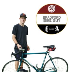 Guy standing behind a bike with a round red and black logo to the right of him that says Bradford Bike Guy