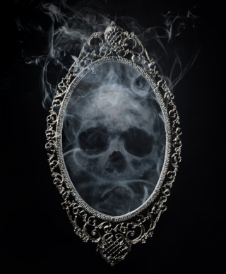 A spooky skull made of wispy smoke looking out at us from a mirror