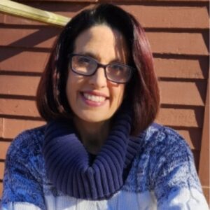 Smiling auburn haired woman in a blue sweater in front of a brown building