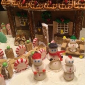 Snowmen and other winter things made out of candy in front of a gingerbread house