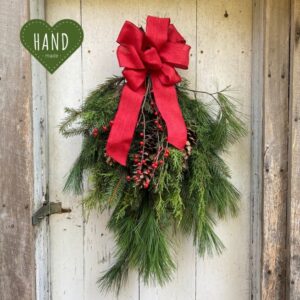 Evergreen Christmas Swag with red ribbon on top hanging on light wood door