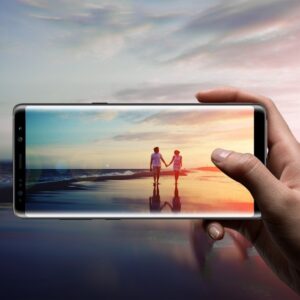 Hand holding up smartphone which is taking a picture of two people walking in a sunset