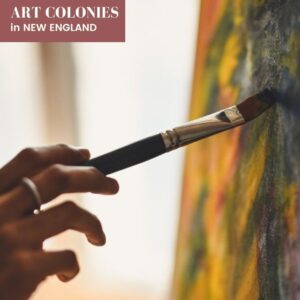 A hand with a ring holding a paintbrush against a yellow and green canvas