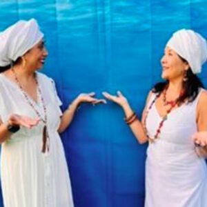 Two women in white dresses and white head coverings looking at each other on a blue watery looking background