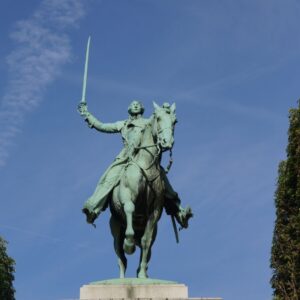 Green metal statue of a man riding a horse holding a sword straight up in the air