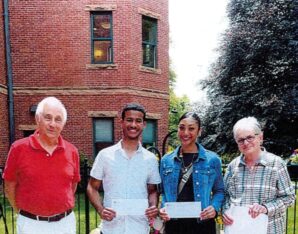 A white haired man, a dark skinned young man, dark skinned young woman, and light skinned white haired woman standing in front of a brick building