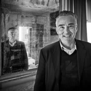 Black and white photo of man smiling in front of a mirror but the same man is frowning in the mirror