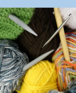 Pile of multicolored wool skeins with knitting needles and a crochet needle sticking out