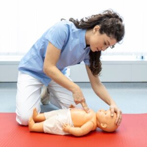 Light skinned woman with brown hair in a blue shirt performing infant CPR on a light skinned doll