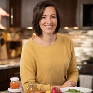 Smiling light skinned dark haired woman in a tan long sleeve shirt