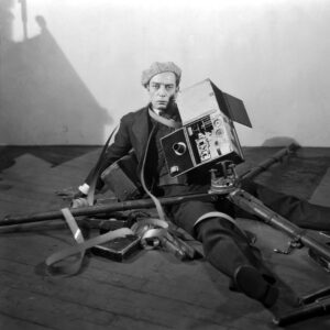 Black and white photo with man sprawled on floor with broken camera around him