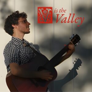 Light skinned man playing guitar with V in the Valley words next to him
