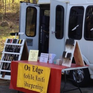 White van with a table out front and a bookcase with knives as well as a sign that says On Edge Knife Sharpening