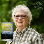 Author Randi 654 Light skinned woman with glasses, a checked shirt, and white hair smiling